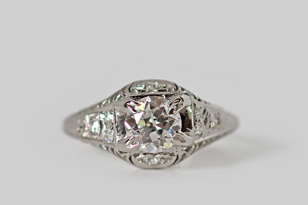 Antique Jewelry Portland, Vintage Jewelry Portland , Antique Engagement Rings | Poor Mouchette | An elegant, Art Deco era engagement ring, modeled in platinum, whose primary gem is a .80 carat Old European cut diamond (E/F, VS1). This antique diamond is held in four pairs of double-prongs. It is exceptionally white, clean, and symmetrical, with a small table, steep crown facets, and an open culet. The setting is replete with intricate decor— tiny, lip-shaped, diamond-set panels decorate its gallery