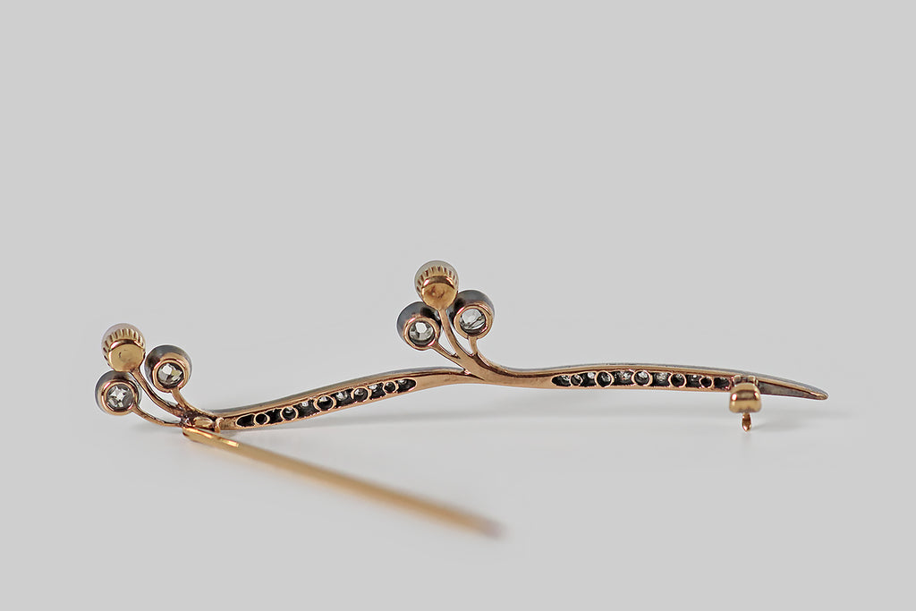 Poor Mouchette | Curated Antique Jewelry, Vintage Jewelry & Engagement Rings | Portland, Oregon | An elegant, Art Nouveau era brooch, modeled in rosy 14k yellow gold with a silver top. This antique brooch takes the form of a graceful stem, with two nodding trefoil blossoms. The ribbon-like stems, here, are bead-set with small old mine cut diamonds that graduate toward the center. The trefoil blossoms are each composed of two larger, bezel-set, early old mine cut diamonds