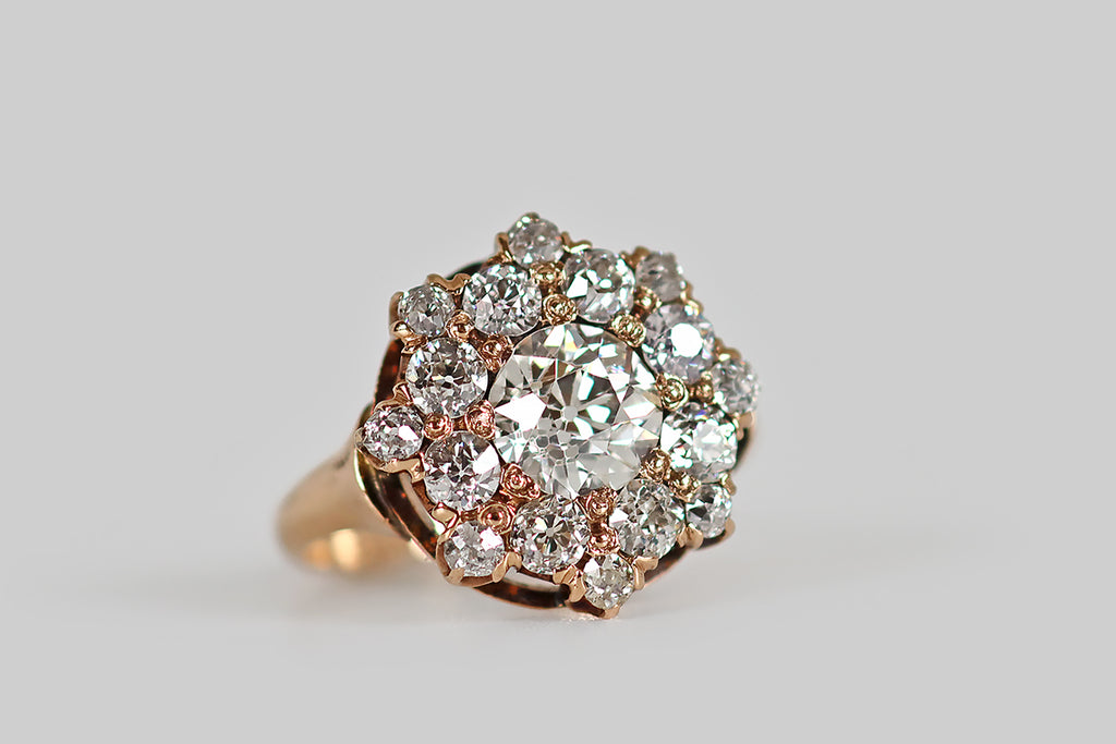 Poor Mouchette | Curated Antique Jewelry, Vintage Jewelry & Engagement Rings | A Victorian era cluster ring, modeled in rosy 14k yellow gold, whose primary gem is a .85 carat old European cut diamond (H, VS2). This central diamond is beautifully cut, with an open culet that reflects repeatedly in the stone's crown facets, creating a striking Kozibe effect! It is surrounded by a halo