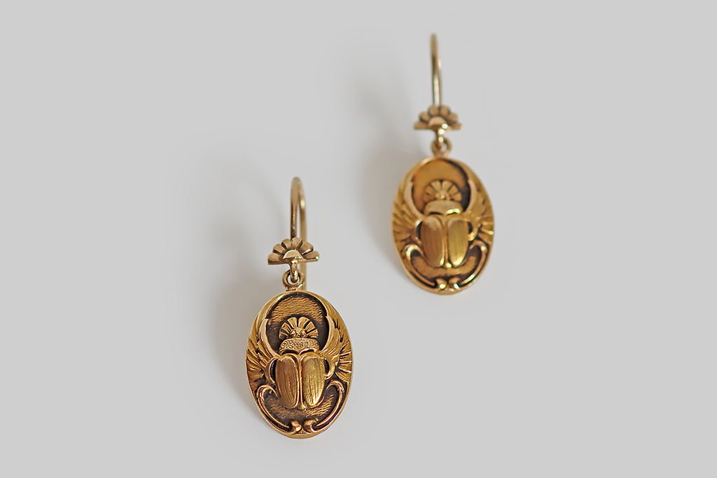 Poor Mouchette | Curated Antique Jewelry, Vintage Jewelry & Engagement Rings | A seriously charming pair of Art Nouveau Egyptian revival earrings, whose oval drops feature a highly detailed and beautifully textured carving of a scarab beetle with open wings. These lovely scarabs hang below a pair of hand-fabricated earwires that are decorated with a motif that repeats the rising sun shape