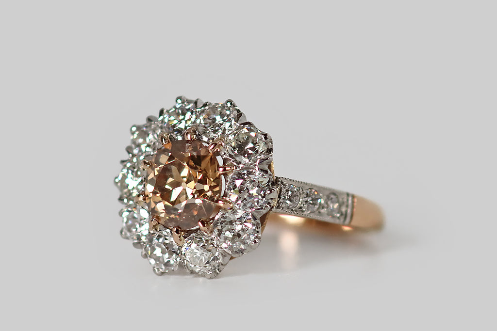 Poor Mouchette | Curated Antique Jewelry, Vintage Jewelry & Engagement Rings | Portland, Oregon | An Edwardian-era, flower-form cluster ring, modeled in 18k rose gold and platinum, whose primary gem is a .90 carat natural, fancy brown, old mine cushion cut diamond. This antique diamond is a beautiful, highly-saturated, peachy-brown color— it is held in ten, tapering rose gold prongs, where it is surrounded by a series of ten white old European cut diamonds.