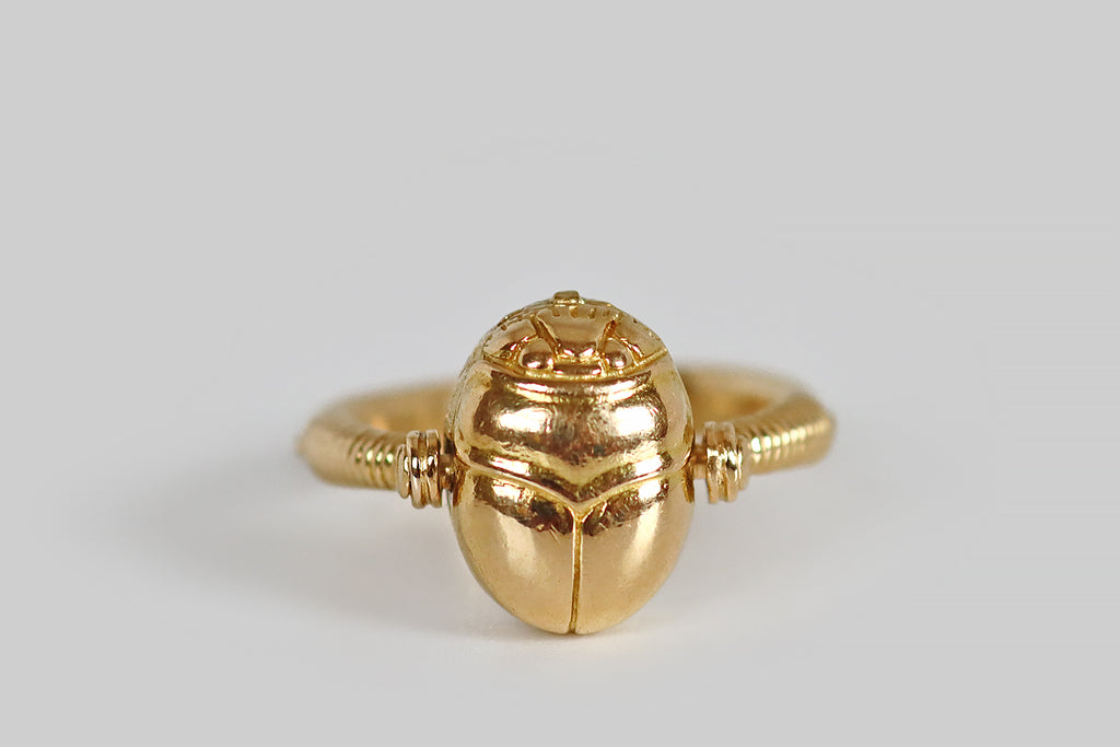 Antique Jewelry Portland, Vintage Jewelry Portland , Antique Engagement Rings | Poor Mouchette | An Art Deco era Egyptian revival ring, modeled in 18k yellow gold, whose head is a three dimensional scarab beetle locket! In the manner of ancient jewelry, this figural ring head rotates, north to south, on a pin that anchors it to the ring's shank. Th top half of our scarab opens to reveal a compartment where you might place a photo, a love note, a scrap of cloth, or a lock of hair. 