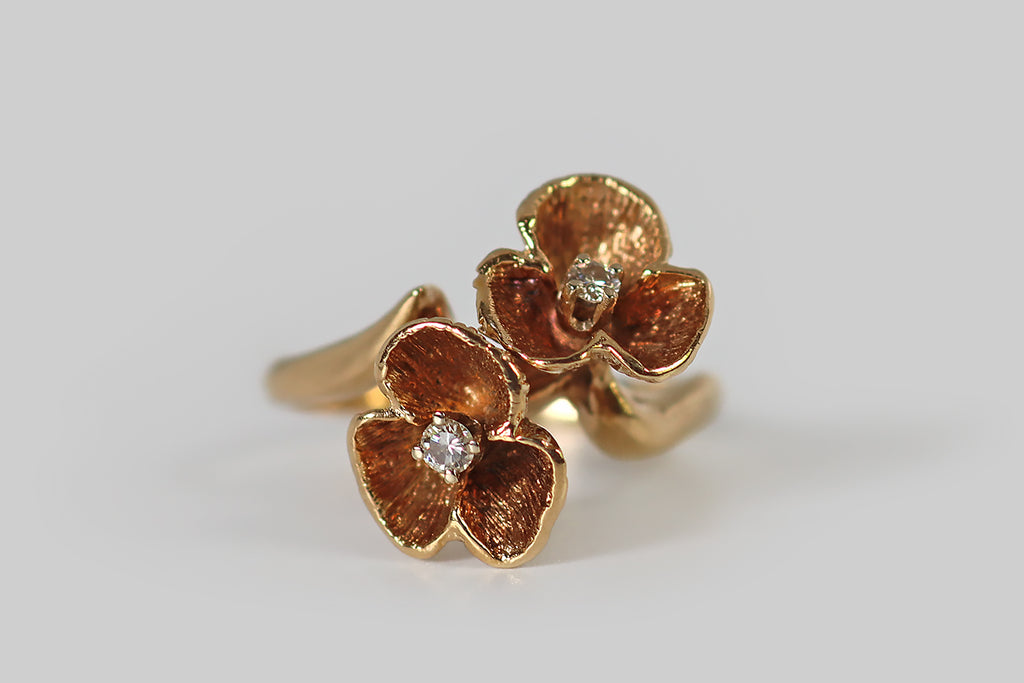 Antique Jewelry Portland, Vintage Jewelry Portland , Antique Engagement Rings | Poor Mouchette | An unusual vintage toi et moi ring, modeled in 14k yellow gold, whose 'you and me' are a pair of three-petaled flowers. These sculptural blossoms are arranged on the diagonal, in a naturalistic manner, atop the ring's curvy, bypass-style shank. The flowers are deeply textured and patinaed, both on their faces and undersides, and each is set with a small, sparkling, brilliant-cut diamond.