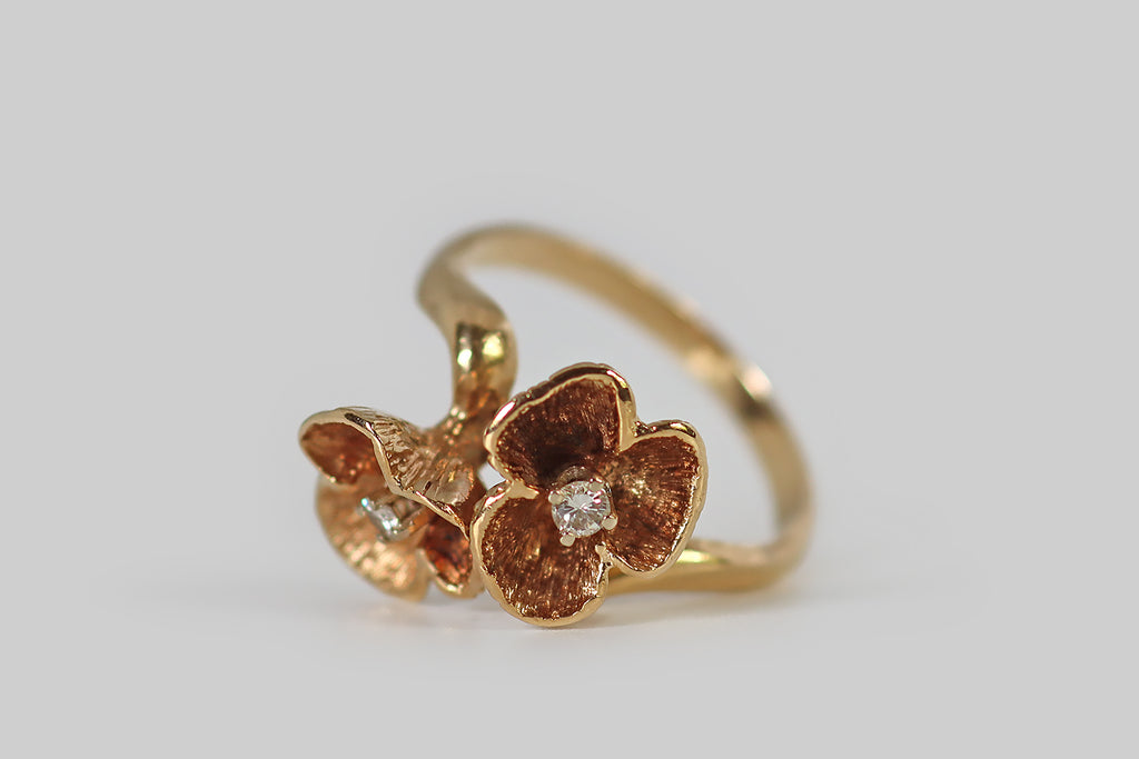 Antique Jewelry Portland, Vintage Jewelry Portland , Antique Engagement Rings | Poor Mouchette | An unusual vintage toi et moi ring, modeled in 14k yellow gold, whose 'you and me' are a pair of three-petaled flowers. These sculptural blossoms are arranged on the diagonal, in a naturalistic manner, atop the ring's curvy, bypass-style shank. The flowers are deeply textured and patinaed, both on their faces and undersides, and each is set with a small, sparkling, brilliant-cut diamond.