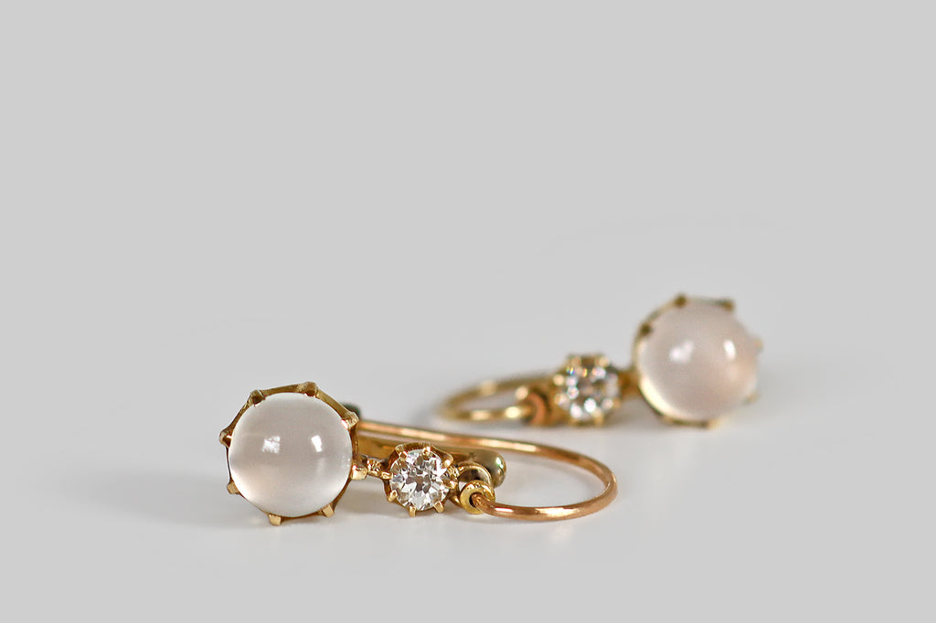 Antique Jewelry Portland, Vintage Jewelry Portland , Antique Engagement Rings | Poor Mouchette | A pair of Victorian-era drop earrings, modeled in 14k yellow gold, whose primary gems are a pair of luminous, white moonstone cabochons. These glowing moonstones are held in crown-like, eight-prong mounts, where they sit below of pair of sparkling, old European cut diamonds, also mounted in prongs.