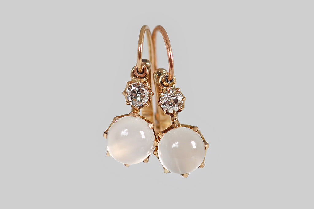 Antique Jewelry Portland, Vintage Jewelry Portland , Antique Engagement Rings | Poor Mouchette | A pair of Victorian-era drop earrings, modeled in 14k yellow gold, whose primary gems are a pair of luminous, white moonstone cabochons. These glowing moonstones are held in crown-like, eight-prong mounts, where they sit below of pair of sparkling, old European cut diamonds, also mounted in prongs.