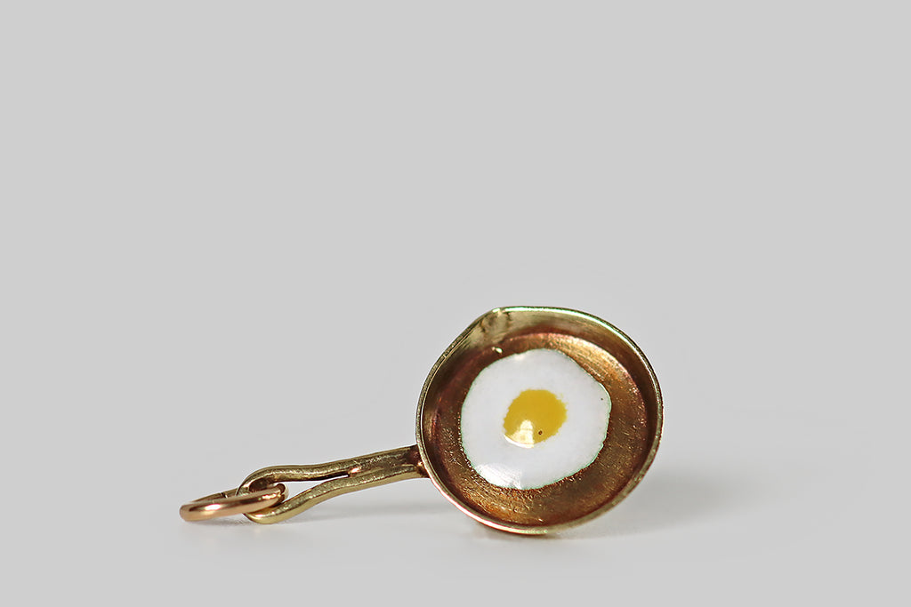 Poor Mouchette | Curated Antique Jewelry, Vintage Jewelry & Engagement Rings | Portland, Oregon | A very cool miniature charm, modeled in 14k yellow gold, made to&nbsp;resemble a frying pan, with a sunny-side-up egg cooking inside it! This little frying pan has an eyelet handle, a patinaed interior, and a pour spout on one side— its egg was created with white and yellow enamel. This was made by the well-known New York jewelers Sloan and Co.
