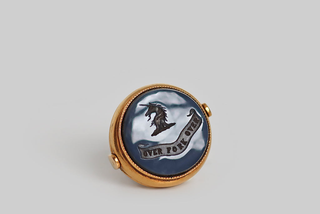 Antique Jewelry Portland, Vintage Jewelry Portland , Antique Engagement Rings | Poor Mouchette | A wonderful, large, Victorian-era fob, modeled in 15k yellow gold and set with an intaglio carved, layered (blue) agate gem. This fine, hand-carved, wax seal is two-sided; it features a unicorn's head on one side, and a monogram (HC) on the other. The unicorn is heroic— shown in profile atop a ribbon base, its beard and mane wave. Below our unicorn's head, a curling banner features the motto "over fork over,"