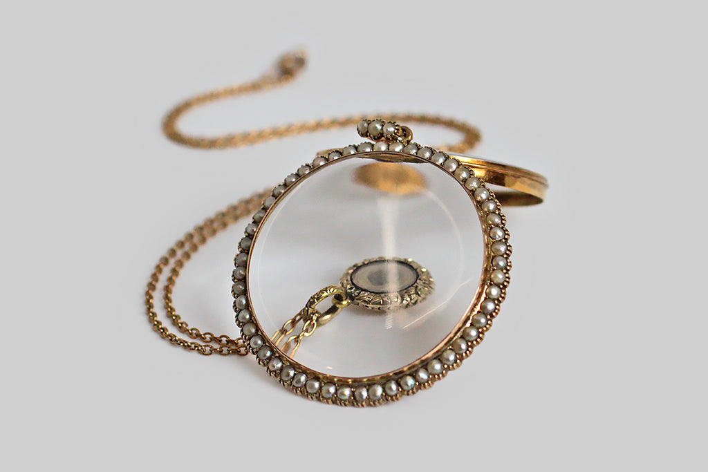 An antique gold locket, made on a grand scale, with a magnifying lens, and a delicate halo of fifty-two, collet-set seed pearls. This airy darling opens easily at the base of the backside, which nests snugly inside the bezel of the front-piece. The locket's large bail is set with three further pearls. This locket is all original. The design is slim and feminine, a perfect frame for whatever treasure is placed inside— a lock of hair, a photograph, a scrap of fabric, a handful of diamonds or colored gems. 